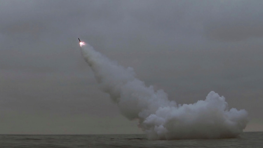 A missile is fired from a submerged submarine into a grey sky. 