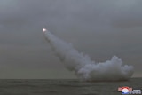 A missile is fired from a submerged submarine into a grey sky. 