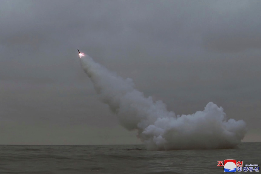 A missile is fired from a submerged submarine into a grey sky. 
