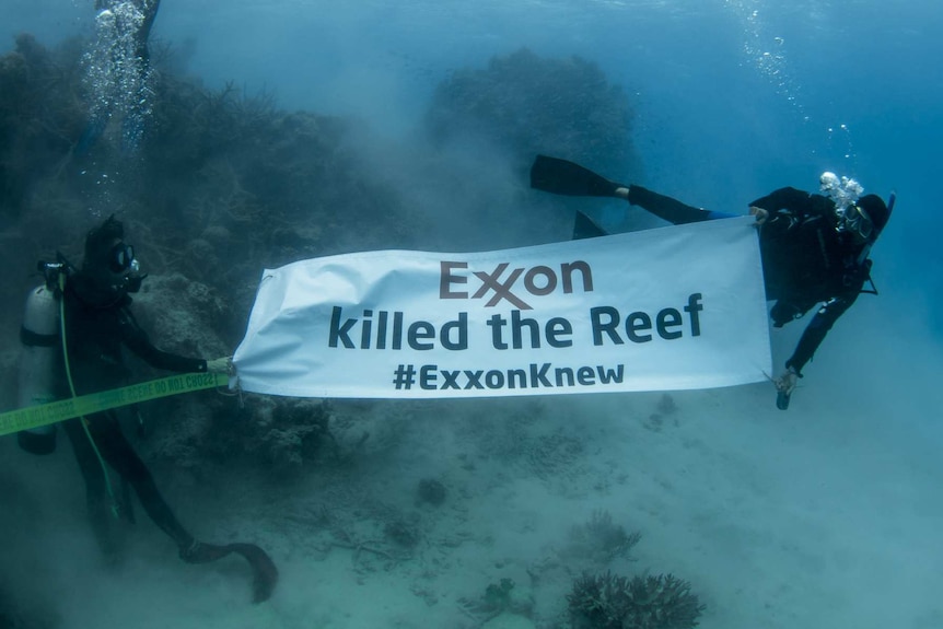 Scuba divers with a sign that reads "Exxon killed the reef #ExxonKnew"