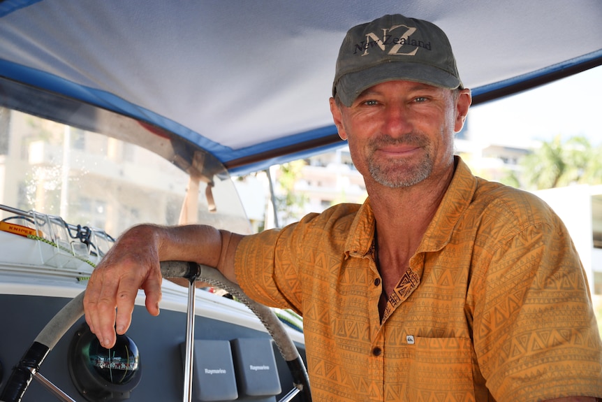 Portrait of a man in a yellow shirt at a boat wheel.