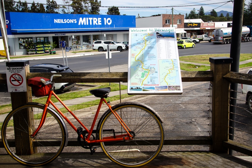 An orange bike is propped up against a mounted map of the town of Bermagui.
