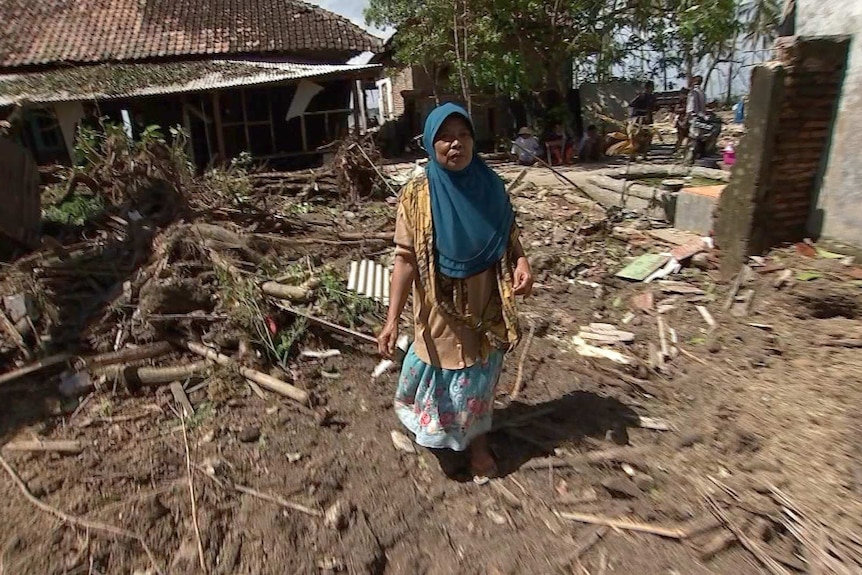 A woman wearing a blue hijab walks through wreckage of buildings