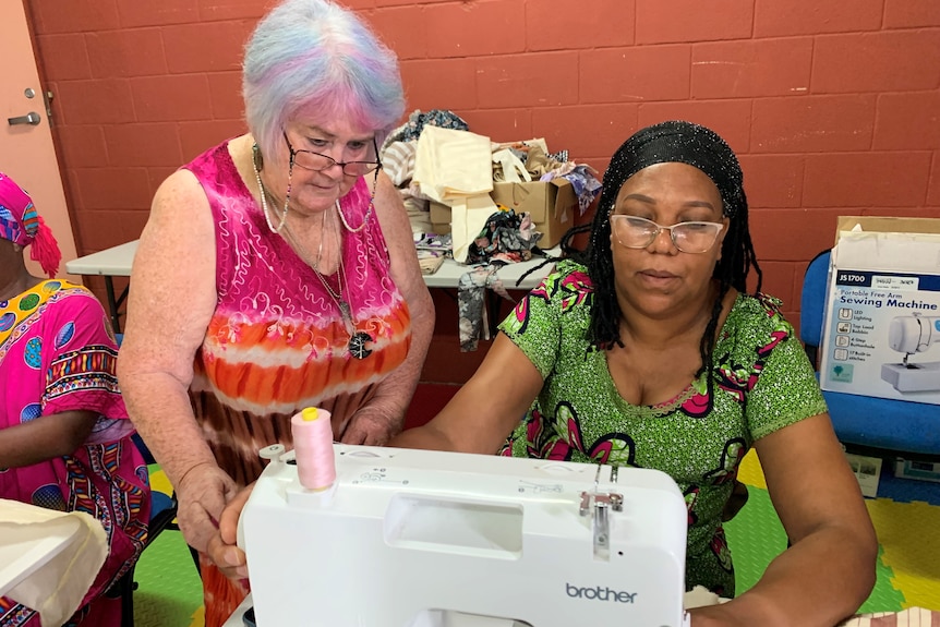 Sewing class teachers watches student Beatrice  Nyamajana on the sewing machine 