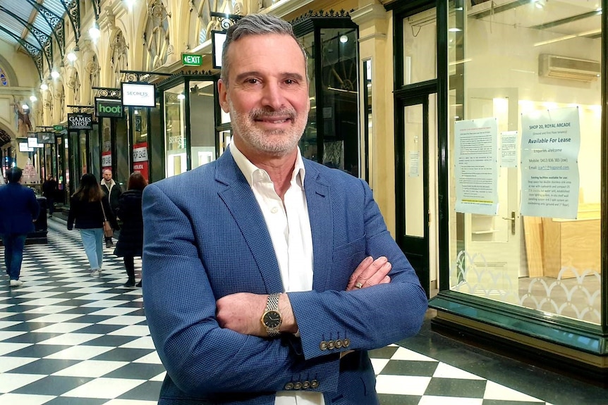 A suited man stands in a shopping arcade.