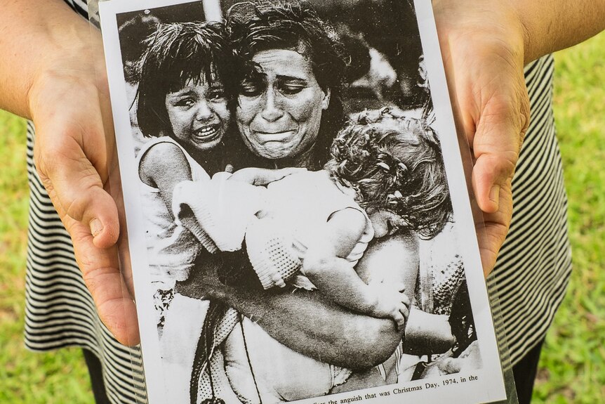 An older woman's hands hold a laminated portrait of her during Cyclone Tracy.