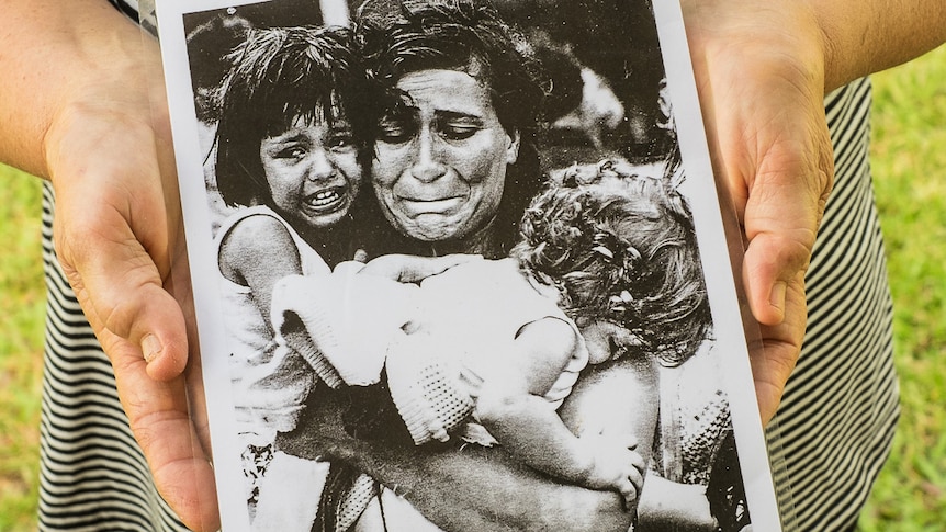 An older woman's hands hold a laminated portrait of her during Cyclone Tracy.