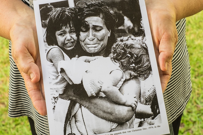 An older woman's hands hold a laminated portrait of her during Cyclone Tracy.