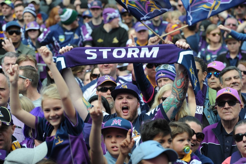 A Melbourne fan holds up a scarf that reads "STORM" in the middle of a packed crowd.
