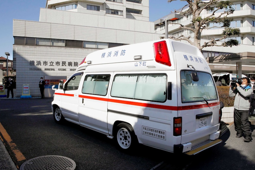 An ambulance pulls into a hospital with masked officials standing outside.