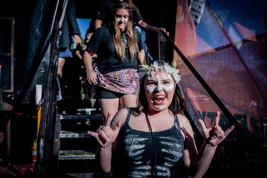 Teenage girl with traditional face paint smiles cheekily as she walks down stage.
