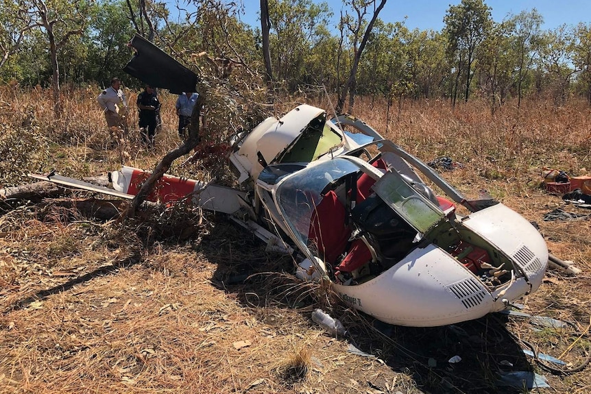 Three people stand around a crashed helicopter in Kakadu.