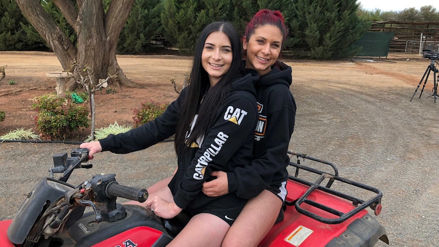 Christina and Irene Vithoulkas sit on a quad bike together on a gravel driveway of a rural property.