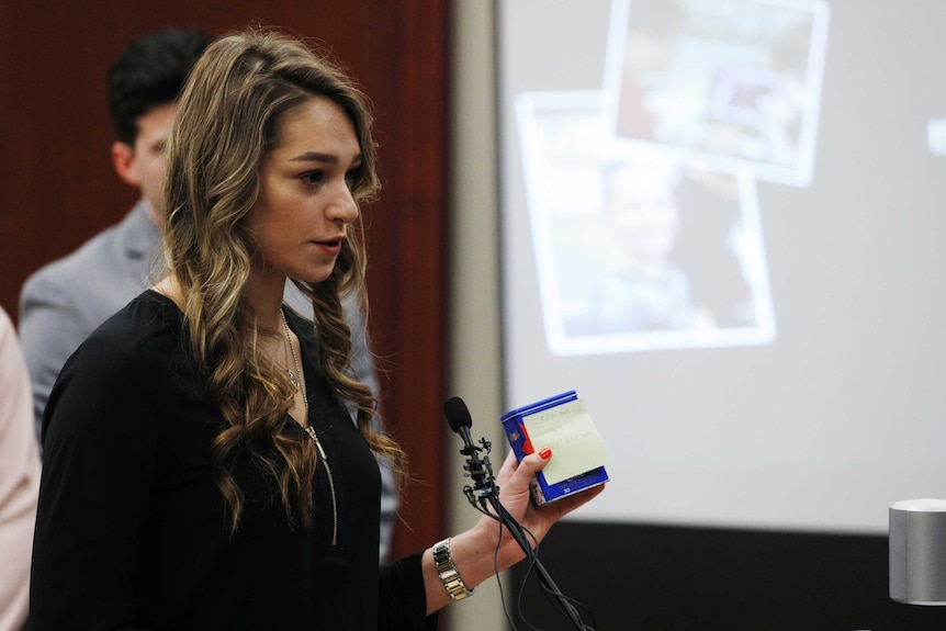 Former gymnast Isabell Hutchins stands behind a microphone in court.