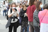 A woman wearing a mask and gloves waits in line outside Centrelink.