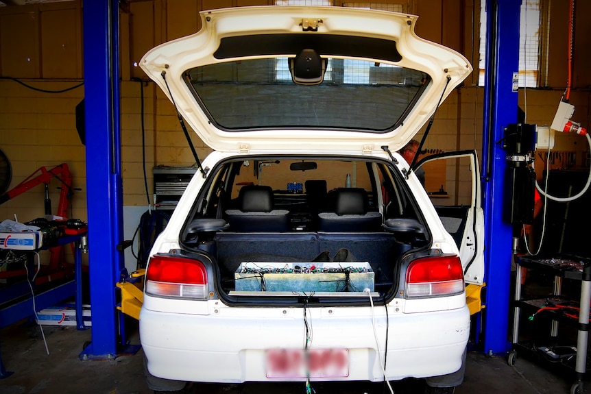 A white car lifted up in a auto electricians workshop with its boot open and a battery pack in the back