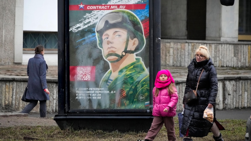 people walk past an army recruitment poster on a street in St Petersburg 