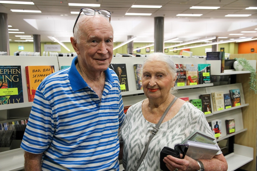 An eldery couple stand together in a public library.