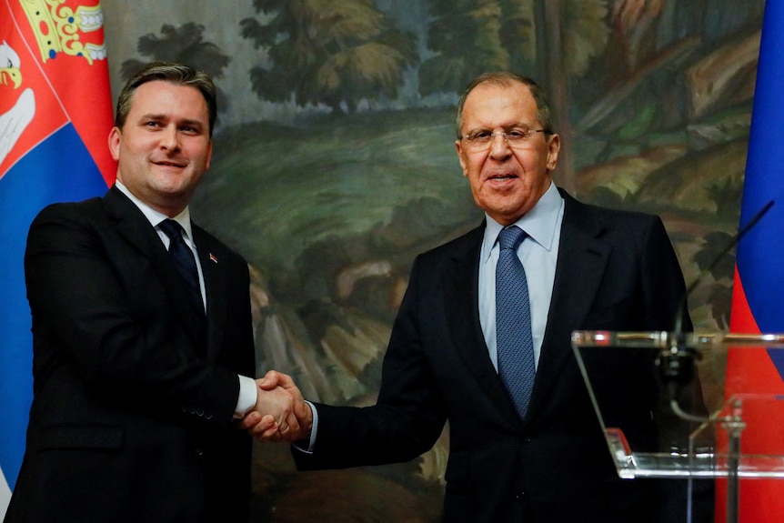 The two minister shake hands with the Russian and Serbian flags partially visible behind them. 
