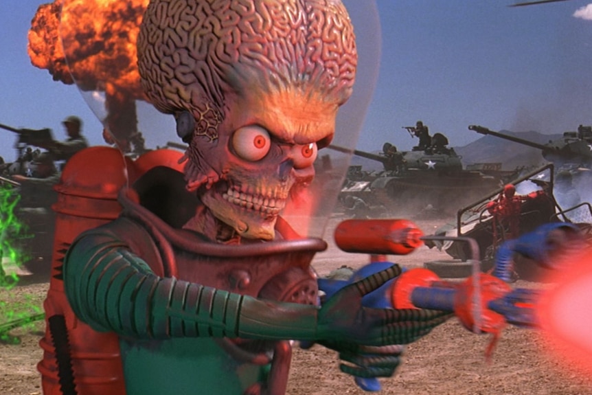 An alien figure with a large brain-like head and angry eyes fires a weapon as a battle rages behind him
