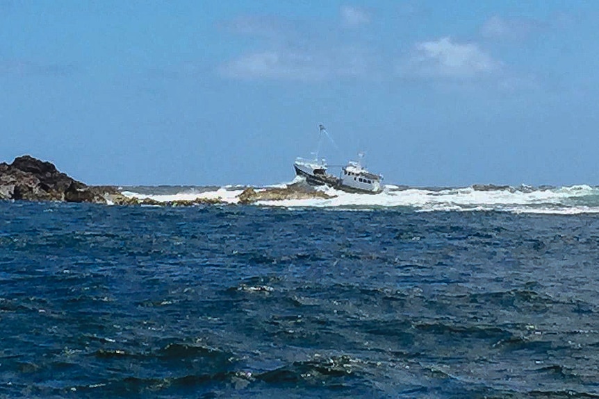 A green cray boat rises bow first over a big wave outside of a rocky cove.