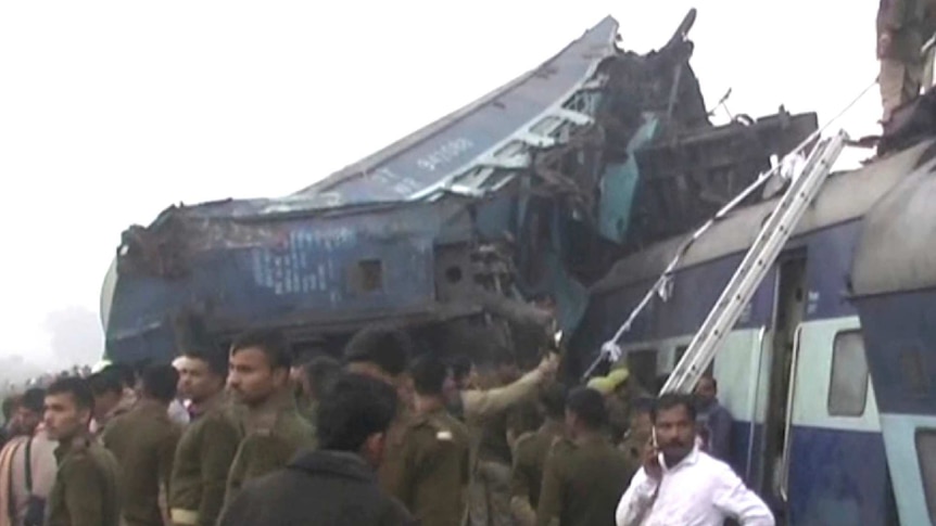 India's security forces personnel gather at the site of a train accident near Pukhrayan, a train is shown mangled and derailed