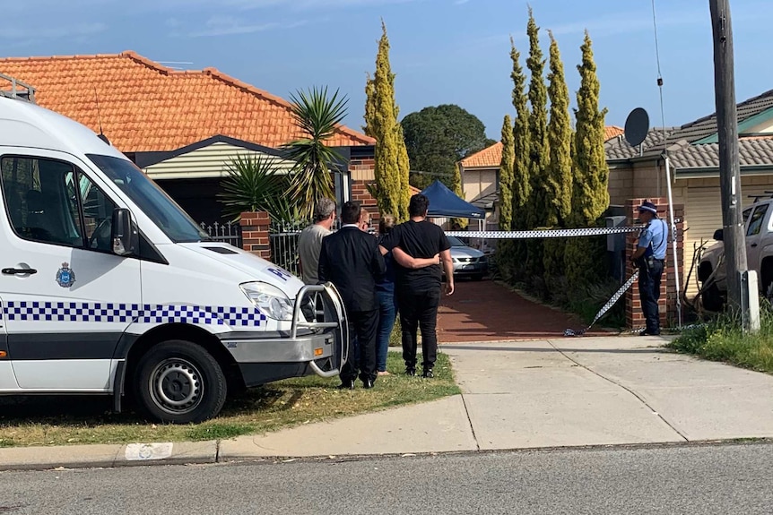 A group of people stand next to a police vehicle looking towards a brick and tile home in Nollamara with police tape across it.