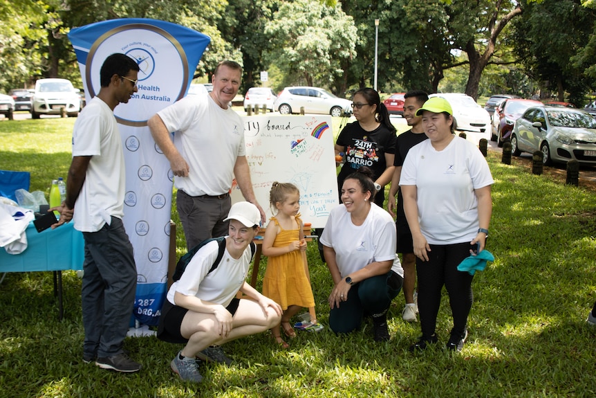 A group of people laugh around a sign at a walk for mental health