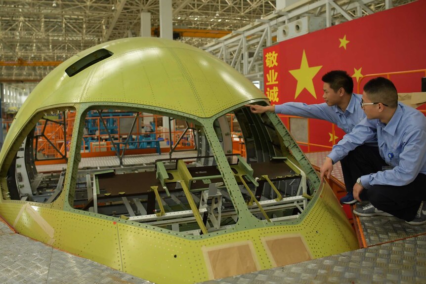 Two men inspect the front of a commercial jetliner in a factory in China.