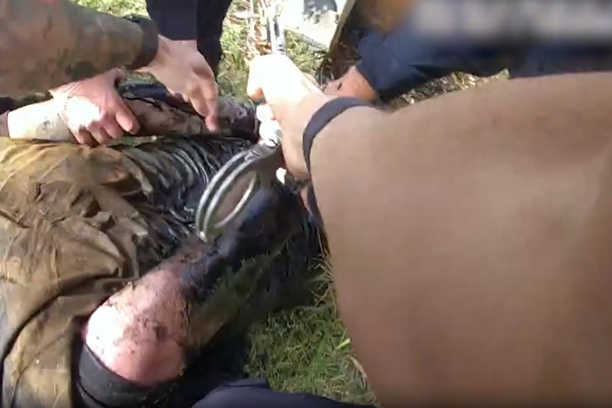 Police place handcuffs on a man who is lying face down on the ground.