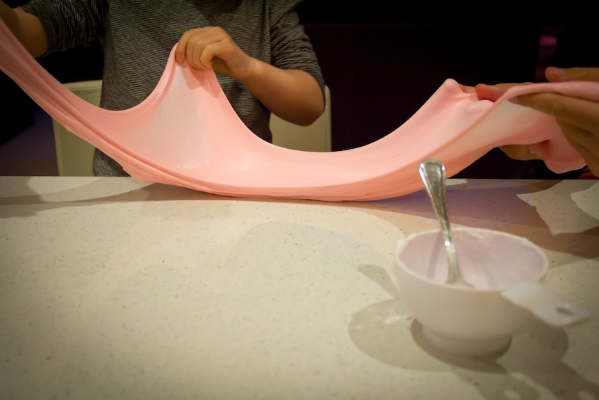 Children stretch pink slime out along a kitchen bench.