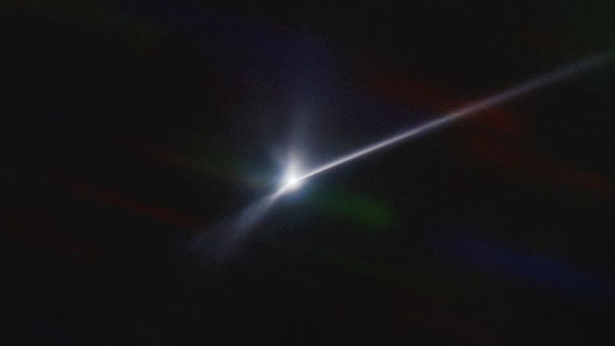 A long, bright white streak is seen on a pitch black background