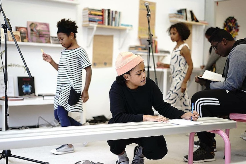 A young woman writes on a bench with children in the background