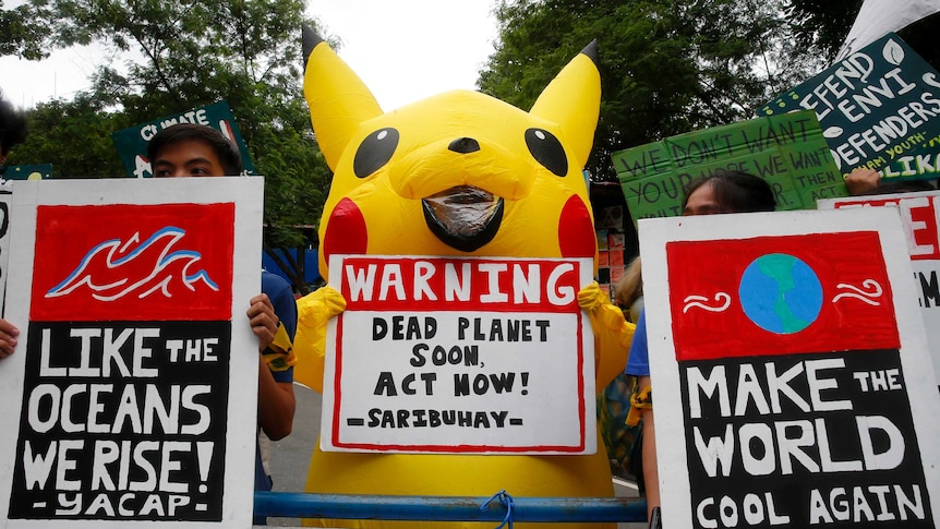 Teenager wearing a Pikachu outfit holding a placard at a climate rally.