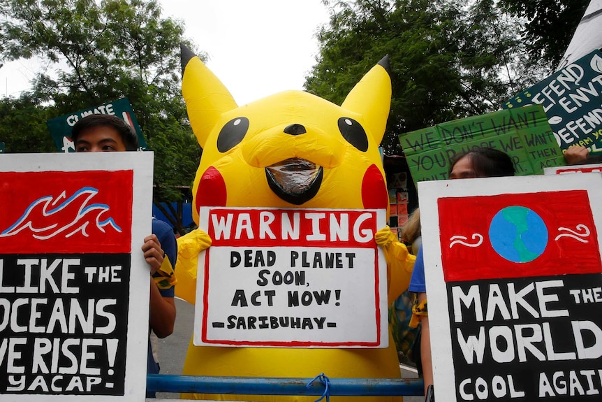 Teenager wearing a Pikachu outfit holding a placard at a climate rally.