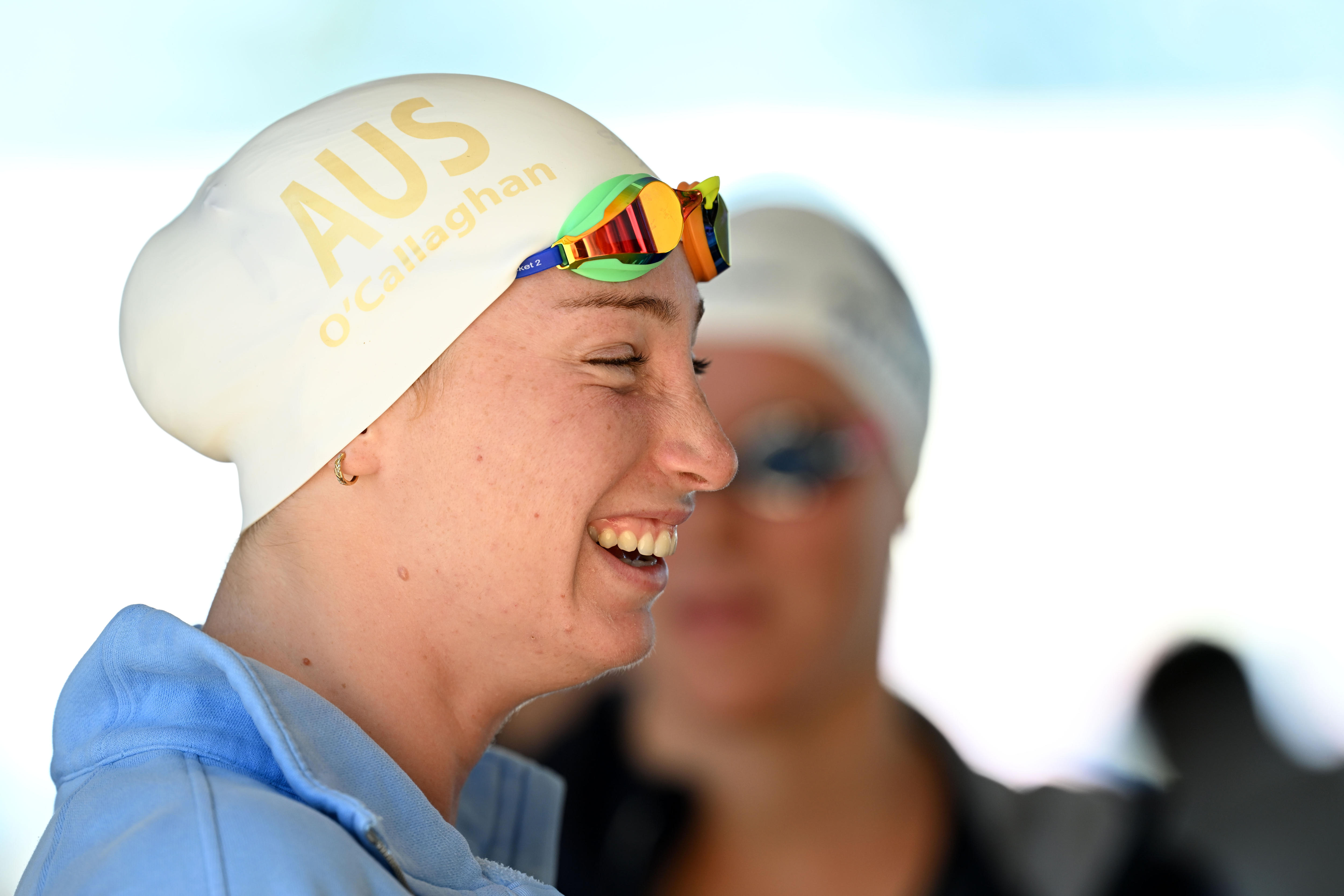 A swimmer in cap and raised goggles laughs.