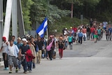 A group of migrants walk along roadside carrying Honduran flag