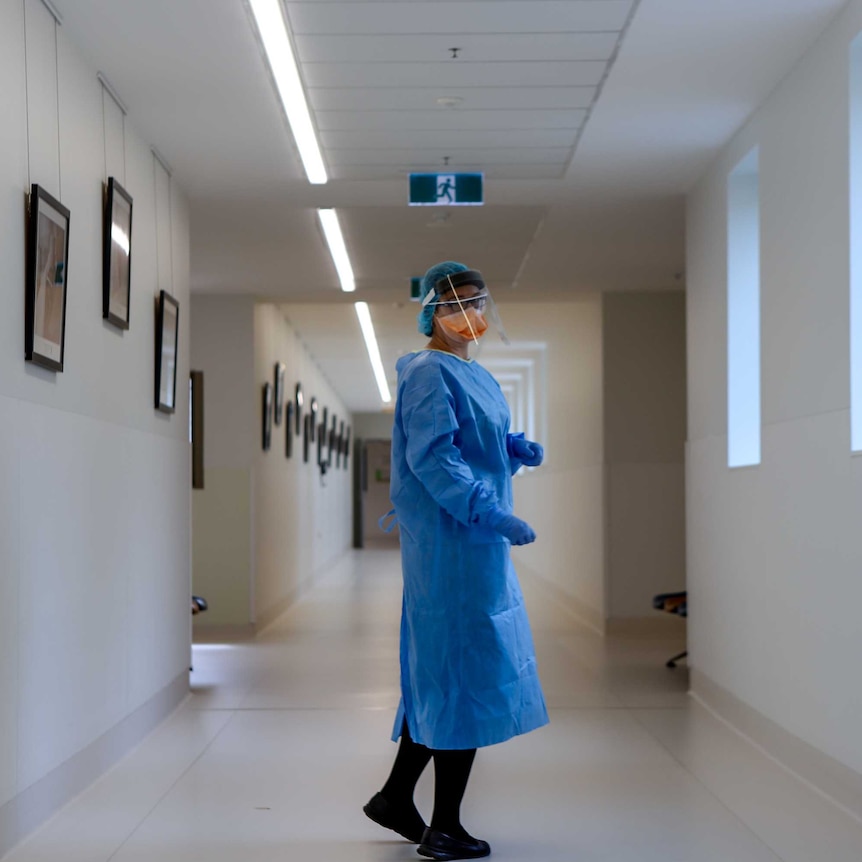 A nurse stands in PPE in a hospital corridor.