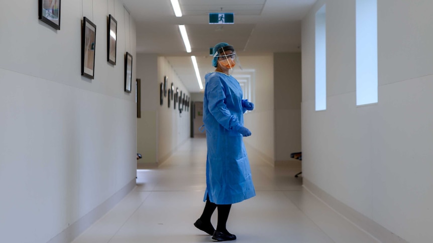 A nurse stands in PPE in a hospital corridor.