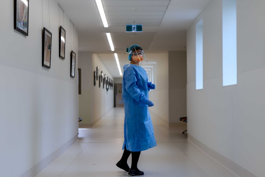 A nurse stands in PPE in a hospital corridor.
