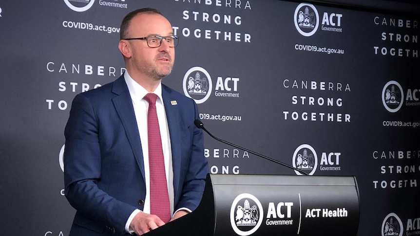 A suited man talks at a podium into a microphone.