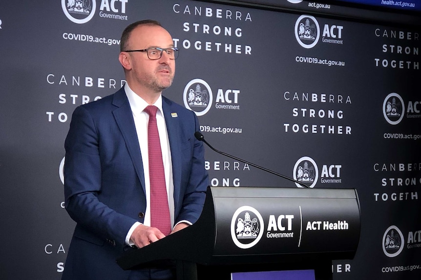 A suited man talks at a podium into a microphone.