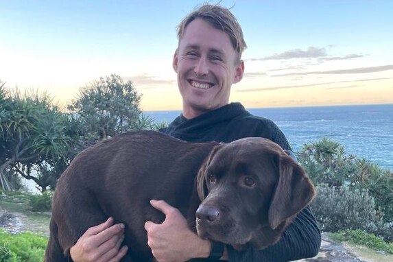 Labuschagne holding a chocolate lab with sunset behind them.