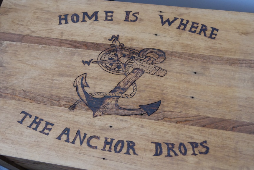 A close up of a wooden box with "home is where the anchor drops" written with an anchor drawing.