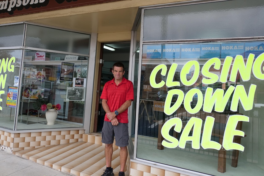 Craig Simpson standing out the front of the store with 'closing down sale' signs on the windows