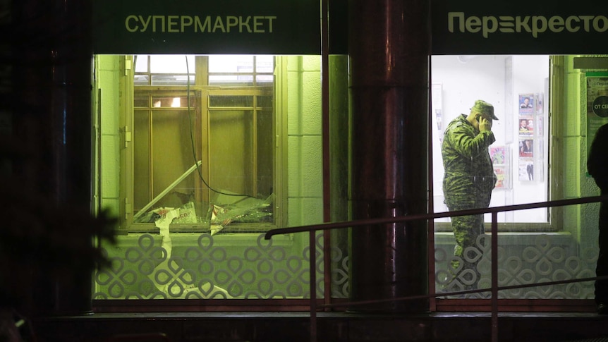An investigator speaks on the phone inside a Russian supermarket, next to a smashed window after an explosion.