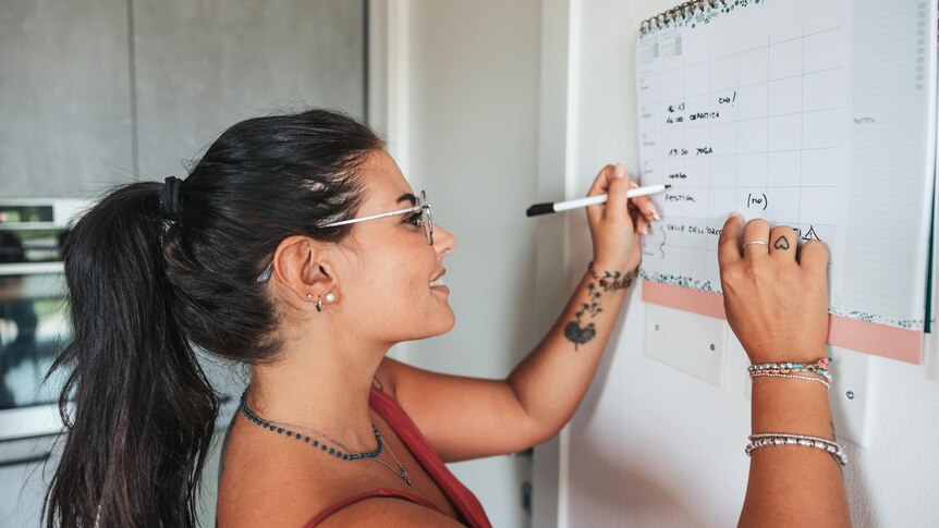 A woman writes on a calendar on her wall