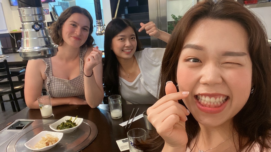 Three friends, including the author, do the Korean love heart fingers sign around a KBBQ table.