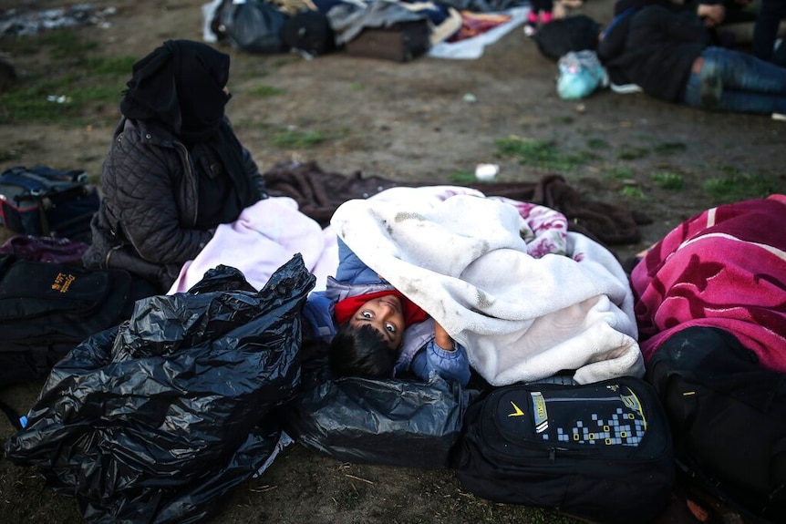 A child sleeping on top of garbage bags with a woman to his right.
