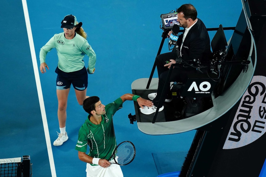 Novak Djokovic looks up at the chair umpire while touching him on the foot.